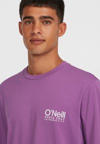Purple long-sleeve t-shirt with crew neck and white logo on left chest, made from soft fabric, featuring a casual, relaxed fit.