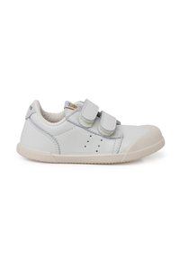 Zapatilla blanca de cuero con dos correas de Velcro, punta redondeada, suela de goma texturizada y pequeños agujeros de ventilación en los lados.