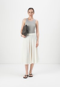 Grå ribbestrikket tanktop, hvit plisserte midiskjørt, svarte flip-flops og en mørkegrå clutch. Glatte materialer, minimalistisk design.