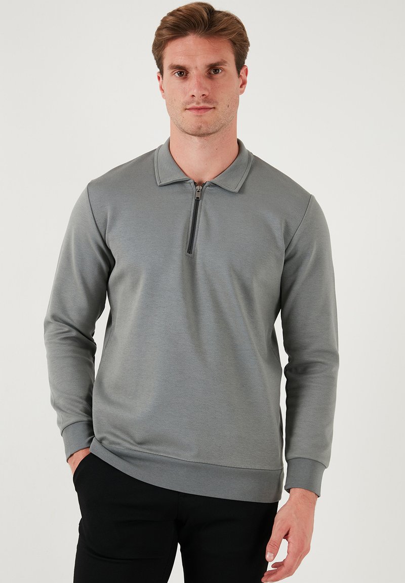 Felpa grigia con zip, maniche lunghe, polsini a costine e colletto. Il tessuto texture conferisce un aspetto moderno, abbinato a pantaloni neri.