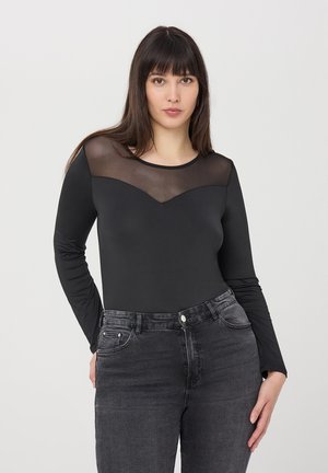 Body lungo nero a maniche lunghe con una scollatura in rete trasparente, abbinato a jeans grigi a vita alta, creando una silhouette strutturata.