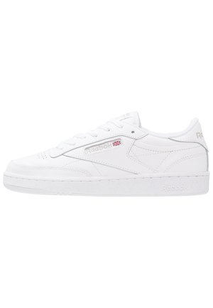Biały niski sneaker Reebok ze sznurowadłami, logo Reebok i flagą Wielkiej Brytanii z boku oraz teksturowaną podeszwą na białym tle.