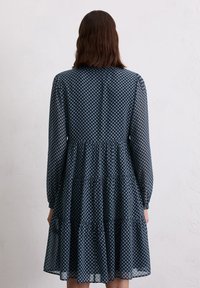 Donkerblauwe jurk met een geometrisch patroon, gelaagde rok, lange mouwen en een ronde halslijn. Semitransparante stof met een vloeiende textuur.