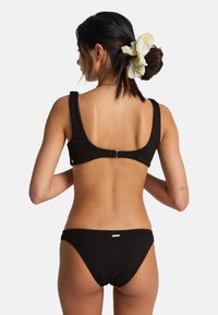 Set bikini nero a costine con scollo quadrato e chiusura regolabile sul retro, completato da slip abbinato con un dettaglio di marchio discreto.