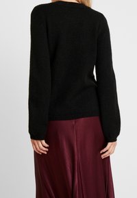 Pull noir en maille avec un col rond et des manches longues, doté de poignets et d'un ourlet côtelés, associé à une jupe en satin bordeaux foncé.