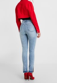 Červená zkrácená bunda přes černý top, kombinovaná se světle modrými džínami s vysokým pasem a bočními rozparky, doplněná červenými lodičkami na vysokém podpatku.