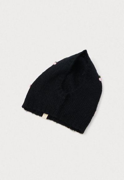 Black knitted beanie with a textured finish, featuring small pink and green fabric accents and a beige tag at the base.