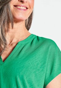 Groene, kortlopende V-hals top van zachte, lichte stof met een iets doorschijnende textuur, die een schone en eenvoudige uitstraling heeft.