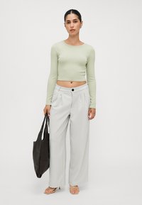 Light green long-sleeve crop top, gray wide-leg trousers with a button closure, and a dark tote bag. Model wearing beige strappy sandals.