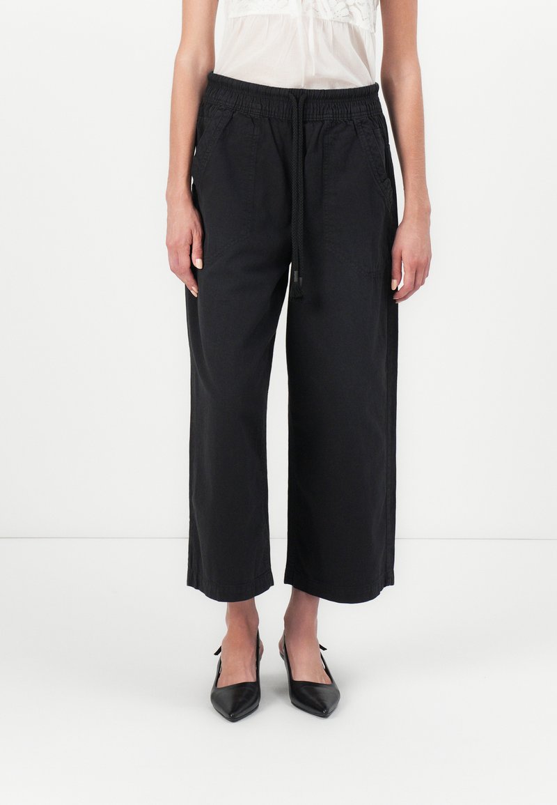 Zwarte, wijde broek met een elastische tailleband en trekkoord. Gemaakt van zachte stof, met zijzakken en een ontspannen pasvorm.