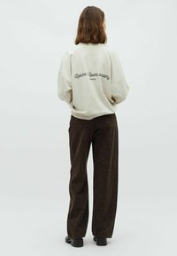 Hellgrauer, übergroßer Sweatshirt mit schwarzem Text auf der Rückseite; kombiniert mit dunkelbraunen, gemusterten weit geschnittenen Hosen mit Zebra-Streifen-Design.