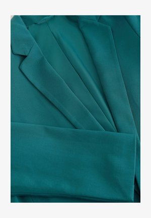 Türkiisi bleiser, millel on sile tekstuur, struktuursed kraed ja kohandatud disain, millel on volditud varrukad ja puhtad jooned.