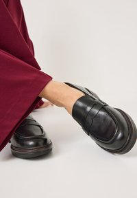 Zwarte leren loafers met een gladde textuur, voorzien van een brede strikaccent en een ronde neus, gecombineerd met burgundy wijde broek.