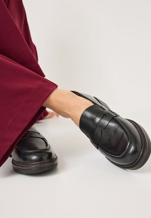 Zwarte leren loafers met een gladde textuur, voorzien van een brede strikaccent en een ronde neus, gecombineerd met burgundy wijde broek.