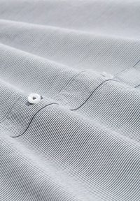 Gestreepte stof met dunne marineblauwe en witte lijnen, met een gladde textuur, waarin een knoopdetail van witte plastic is uitgelicht.