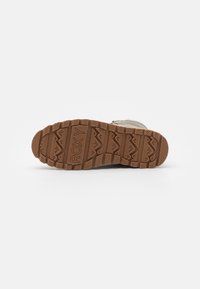 Semelle en caoutchouc beige avec un motif de texture. La tige est en matériau doux de couleur claire avec une finition lisse.