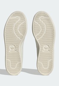 Cream-colored sneaker soles with a textured honeycomb pattern, featuring an Adidas logo at the heel and a wavy design along the sides.