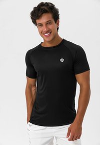 Musta urheilu t-paita, joka on valmistettu sileästä ja kevyestä kankaasta. Ominaisuudet pyöreä pääntie ja lyhyet raglan-hihat, joissa on pieni valkoinen logo rinnassa.