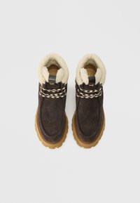 Bruine suède enkellaarsjes met een crèmekleurige fleece voering, decoratieve veters en een gestructureerde rubberen zool. Bevat een gouden logo accent op de hak.