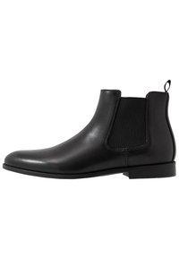 Botte chelsea en cuir noir dotée de panneaux latéraux élastiques, d'une finition lisse et d'une languette au talon. Talon bas avec un design minimaliste.