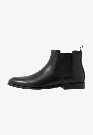 Botte chelsea en cuir noir dotée de panneaux latéraux élastiques, d'une finition lisse et d'une languette au talon. Talon bas avec un design minimaliste.