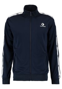 Marinblå zip-up träningsjacka gjord av glatt tyg, med vita sidostråk och upprepade logomönster samt ståkrage.