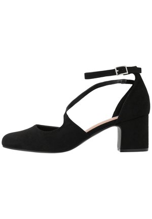 Black suede block-heeled shoes with a pointed toe, ankle strap, and cut-out design, featuring a smooth texture and minimalistic hardware.