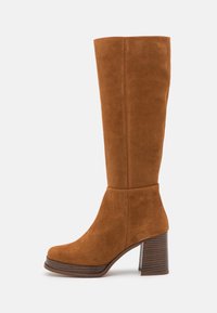 Stivale in suede marrone alto fino al ginocchio con tacco spesso, punta arrotondata e suola con texture legnosa a contrasto. Texture liscia; dettagli di cucitura minimi.