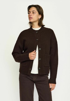 Braun gestrickte Strickjacke mit rundem Halsausschnitt, vorderer Knopfleiste, gerippten Bündchen und zwei vorderen Taschen. Der Stoff sieht weich und strukturiert aus.