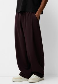 Breda, löst sittande byxor i djup burgundy-färg med elastisk midja och sidofickor, tillsammans med ljusa sneakers. Slät tygstruktur.