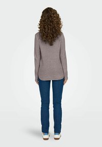 Pull en tricot gris à manches longues, avec un ourlet arrondi. Associé à un jean bleu ajusté et des baskets blanches. Le tissu texturé est visible.