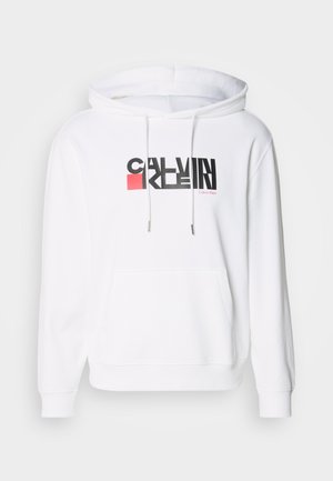 White hooded sweatshirt with front pocket, featuring black and red "CALVIN KLEIN" logo. Drawstrings with silver metal tips, soft texture.