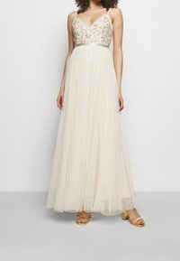 Maxi šaty s květinově vyšívaným korzetem, V-výstřihem a průhlednou sukní s puntíky. Mají nastavitelné ramínka a stříbrný detail v pase.