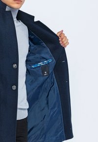 Marineblauwe wollen jas met een knoopsluiting aan de voorkant, uitgerust met een gladde blauwe voering en een zak met een metallic accent. Ontwerp met een casual fit.