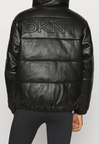 Veste en cuir noir matelassée avec un design quilté, dotée d'un logo en relief bien en vue dans le dos et d'un ourlet froncé pour un ajustement confortable.