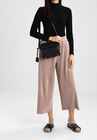 Black long-sleeve top, light pink wide-leg pleated pants, black crossbody bag, and black slide sandals with thick straps. Smooth textures.
