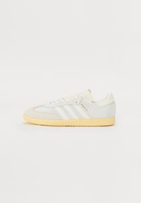 White and beige sneaker with suede and mesh upper, three white stripes, and yellow rubber outsole. Features classic lace-up design and padded collar.