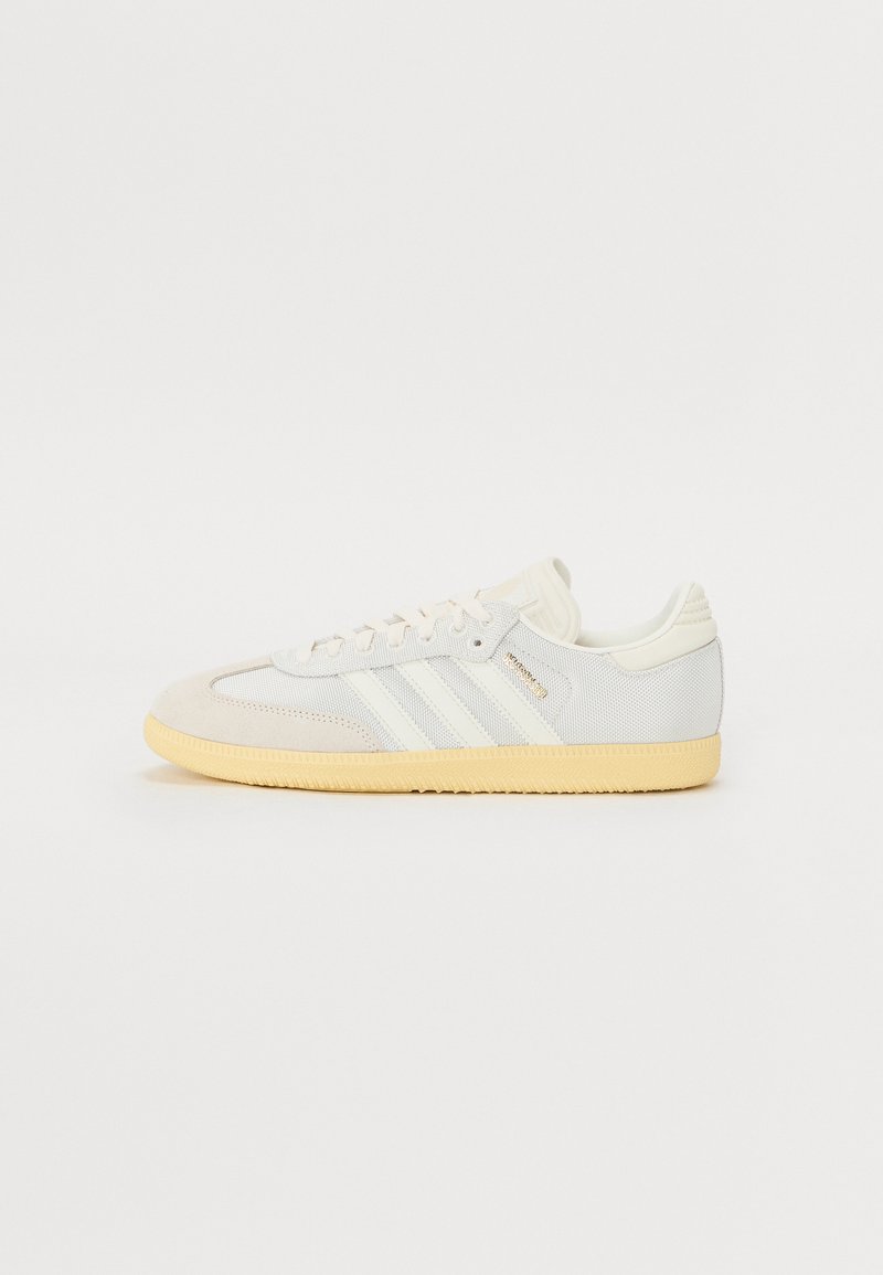 White and beige sneaker with suede and mesh upper, three white stripes, and yellow rubber outsole. Features classic lace-up design and padded collar.