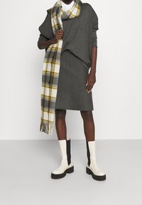 Jersey gris de gran tamaño, falda gris, bufanda de cuadros en amarillo y blanco, y botas altas de dos tonos con acentos negros y suelas gruesas.