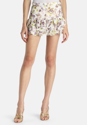 Hvid mini nederdel med blomsterprint og lagdelte flæser, båret med gyldne sandaler med høj hæl og stropper, vist fra talje til fod.