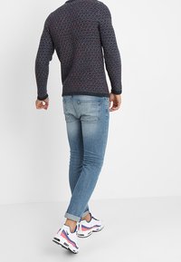 Granatowy sweter o fakturze, jasnoniebieskie dopasowane dżinsy, białe i różowe buty sportowe. Szczegóły obejmują podwinięte mankiety i minimalne szwy.