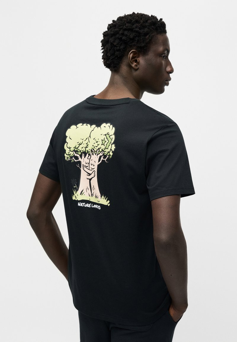 Maglietta nera in cotone con grafica di un albero cartoon verde chiaro sul retro e scritta "NATURE LOVERS" in basso. Maniche corte, scollo rotondo.