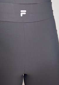 Leggings cinzas com textura canalé e uma cintura larga, apresentando um logo branco, exibindo uma textura suave e um design justo.