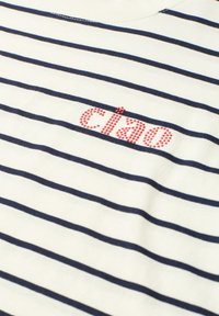 Chemise blanche avec des rayures horizontales bleu marine et texte rouge pointillé "ciao" près de la zone de la poitrine.