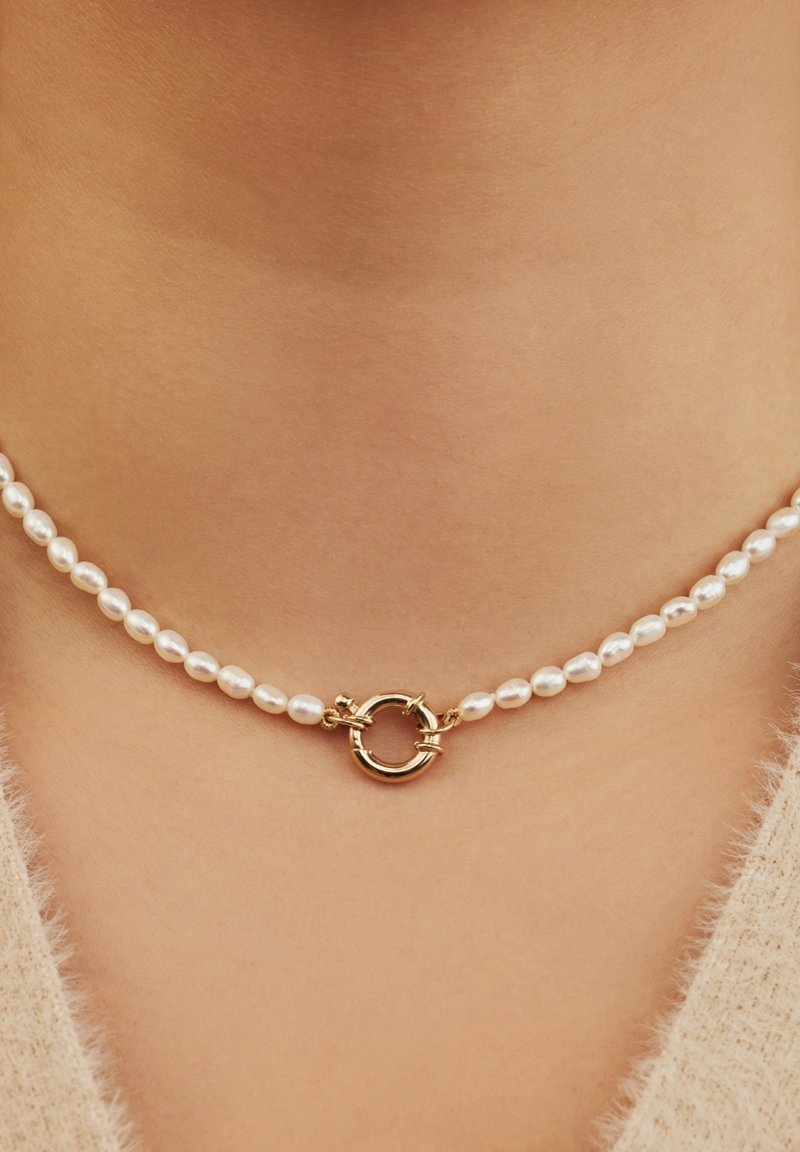Collier ras du cou en perles de culture, composé de petites perles blanches polies et d'un fermoir circulaire doré central avec des accents en boucle.
