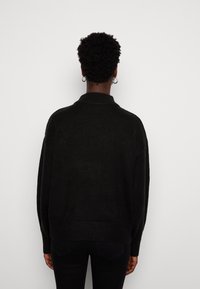 Pull noir oversize avec col montant et épaules tombantes, doté d'un ourlet et de poignets côtelés, vu de dos.