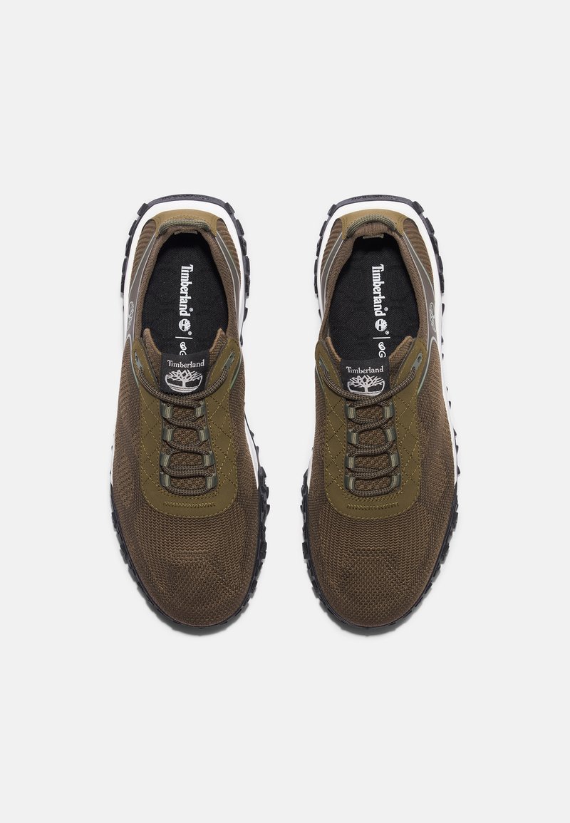 Zapatillas de tejido marrón con parte superior texturizada, diseño de cordones y suela de goma. Presenta el logo de Timberland en la lengüeta y acentos estampados.