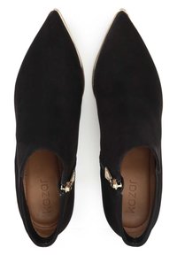 Para czarnych zamszowych botków za kostkę z wydłużonym noskiem i złotym detalem na zamku błyskawicznym oraz brązowymi wkładkami z logo "Kazar" na białym tle.