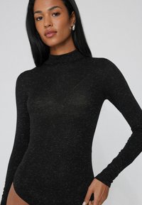 Body a maniche lunghe e collo alto in nero, con una superficie tessile strutturata e sottili venature. Design aderente che mette in risalto la silhouette.