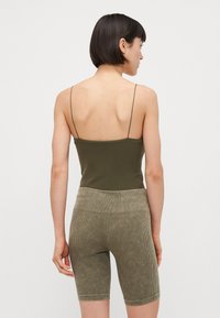 Un débardeur ajusté vert olive à fines bretelles associé à un short de vélo à côtes assorti. La tenue se compose d'un tissu doux et texturé.
